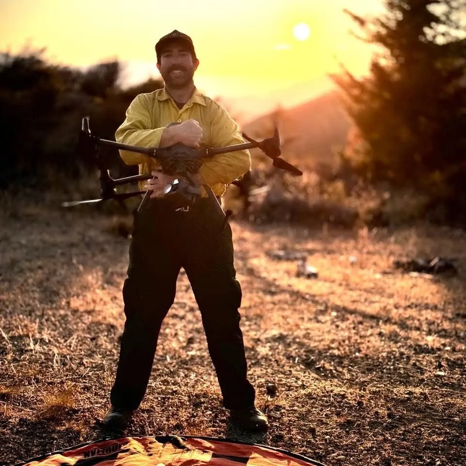 Eli Polsky in the yellow fire shirt at sunset, holding the Matrice 100 over the landing pad.