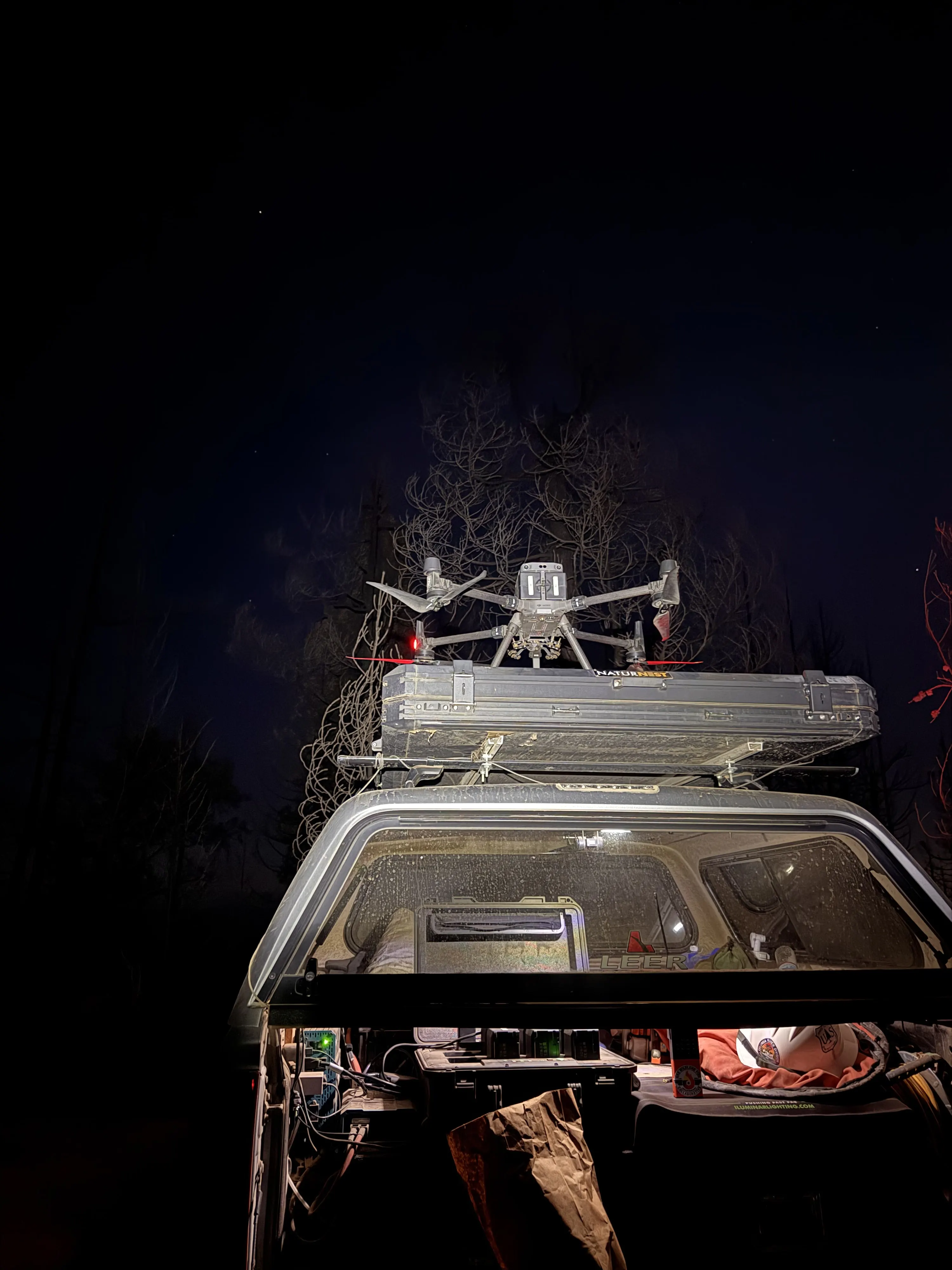 The Matrice 300 launching from the rooftop tent of the truck at night, headlamp lit trees behind it.