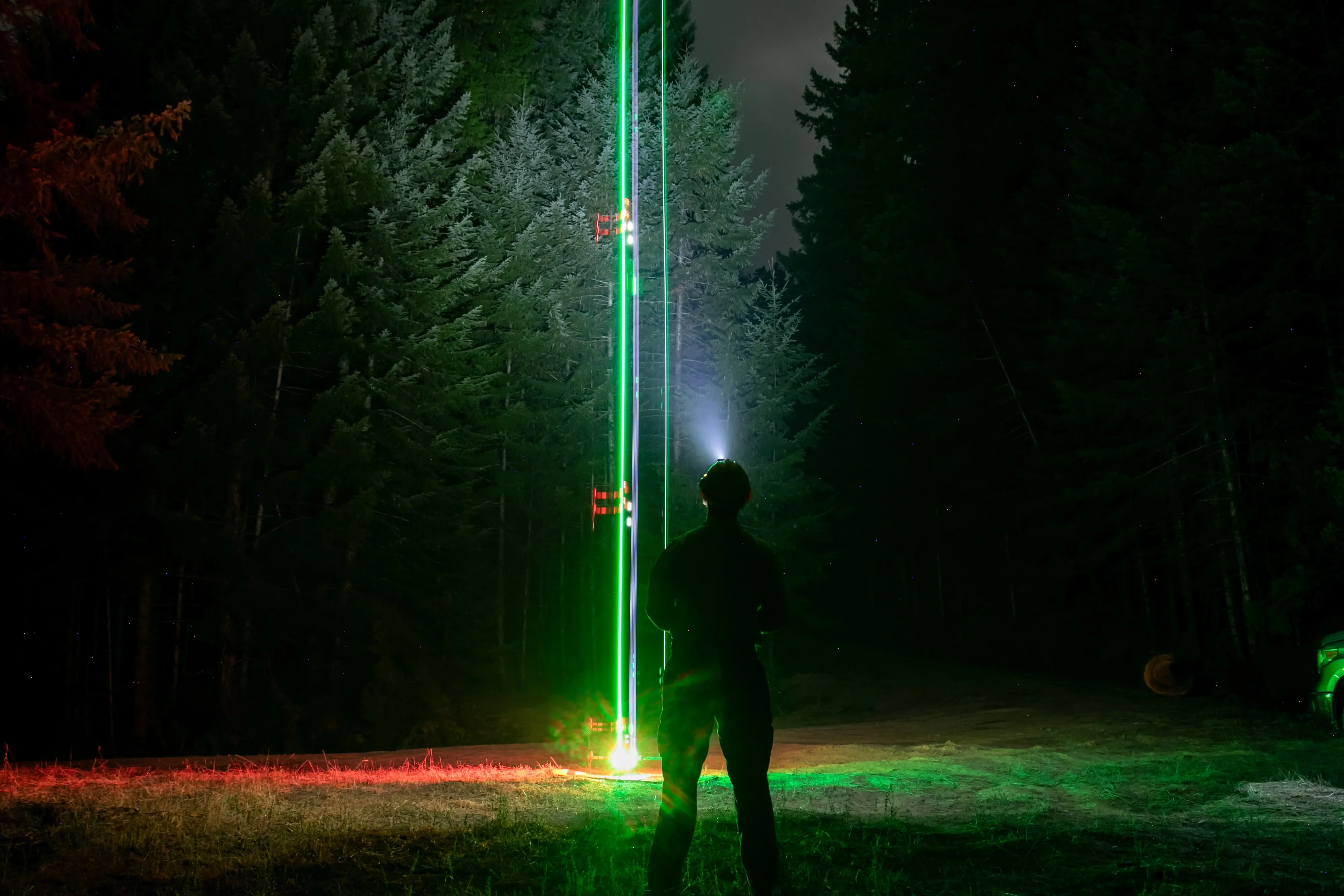 A night launch, the aircraft lights drawn as a green and red trail rising from the launch site, the pilot silhouetted below.