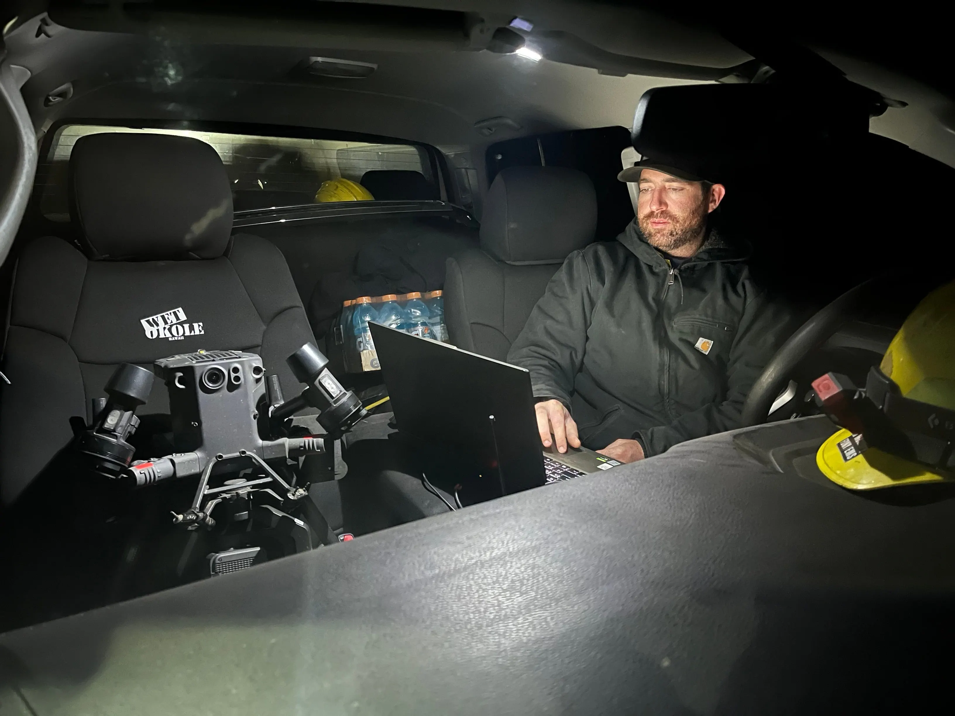 Inside the truck at night, the aircraft on the seat and the pilot working the laptop.